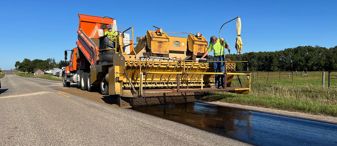 a chip spreader is operated by two workers that are tasked to apply clean aggregate on top of the bitumen as a protective barrier.