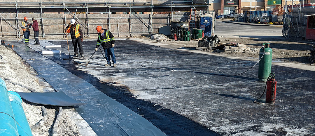 onsite workers are applying waterproofing material to the foundation